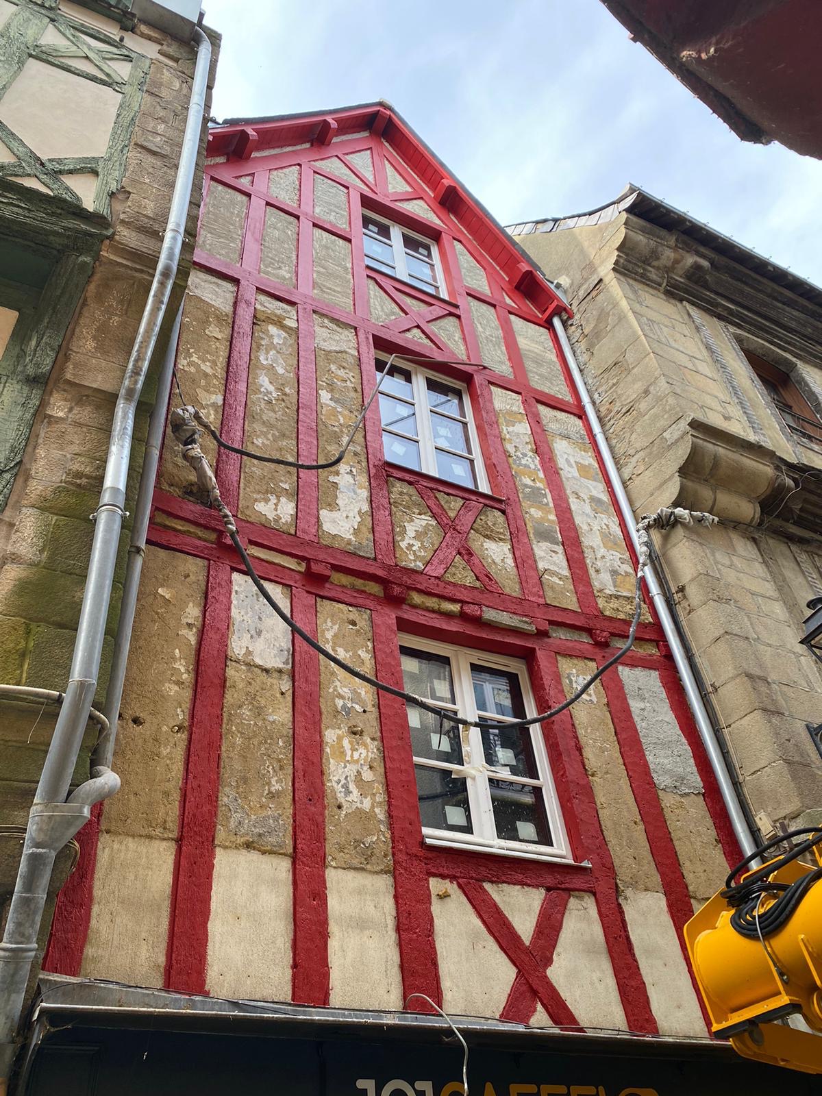 Travaux de peinture sur une maison à colombages. Le bois est peint en rouge.