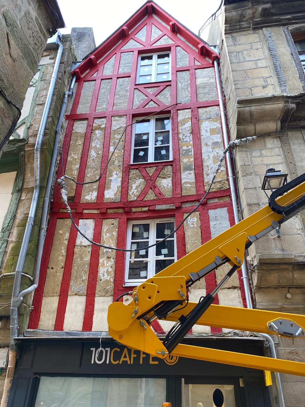 Travaux de peinture sur une maison à colombages. Le bois est peint en rouge.